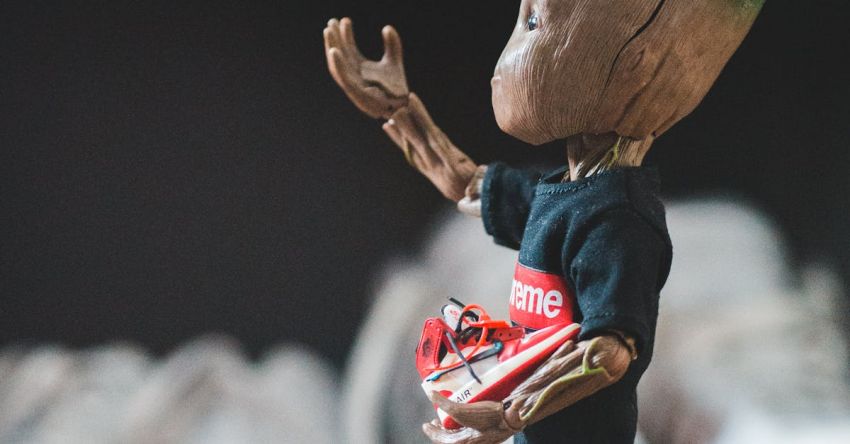 Comic-Con - Crop fan giving small sneakers to small plastic comic tree character dressed in t shirt