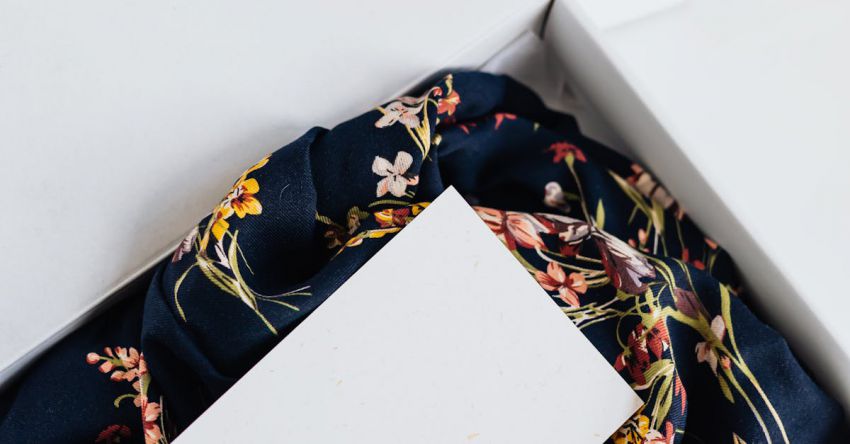 Online Stores - From above of stylish black silk floral pattern cloth with white visit card mockup placed in white carton box after receiving postal delivery of online order